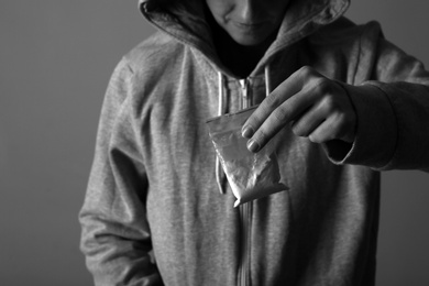 Photo of Drug dealer holding bag with cocaine on dark background, closeup. Black and white effect