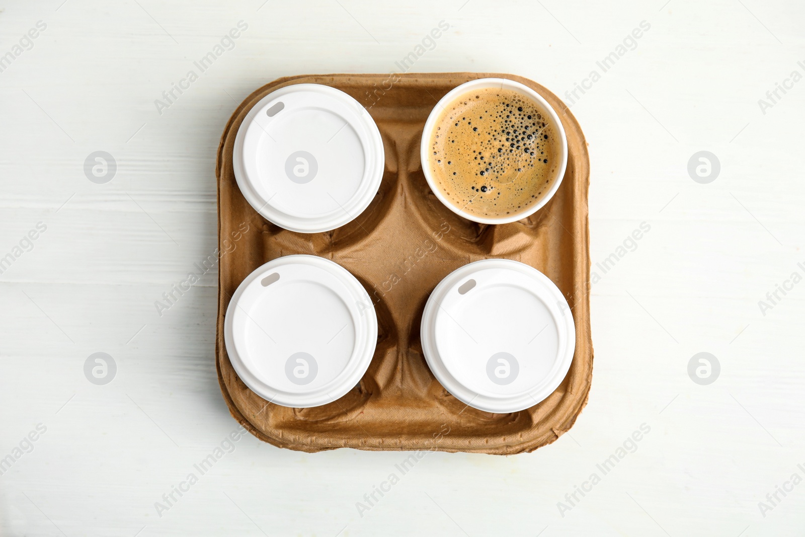 Photo of Takeaway paper coffee cups in cardboard holder on white wooden table, top view