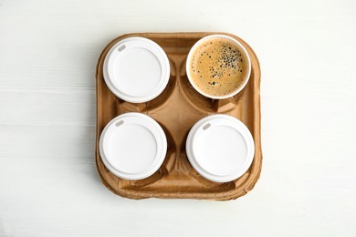 Photo of Takeaway paper coffee cups in cardboard holder on white wooden table, top view