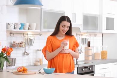 Photo of Beautiful pregnant woman drinking milk in kitchen