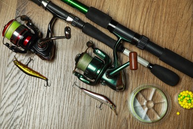 Fishing rods with spinning reels and baits on wooden background, flat lay