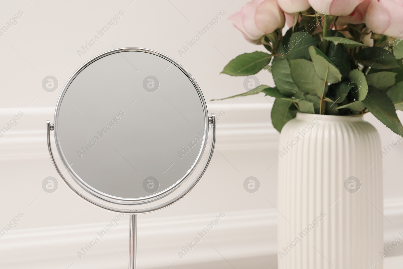 Photo of Mirror and vase with pink roses on dressing table, closeup