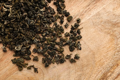 Photo of Heap of dry green tea leaves on wooden table, top view. Space for text