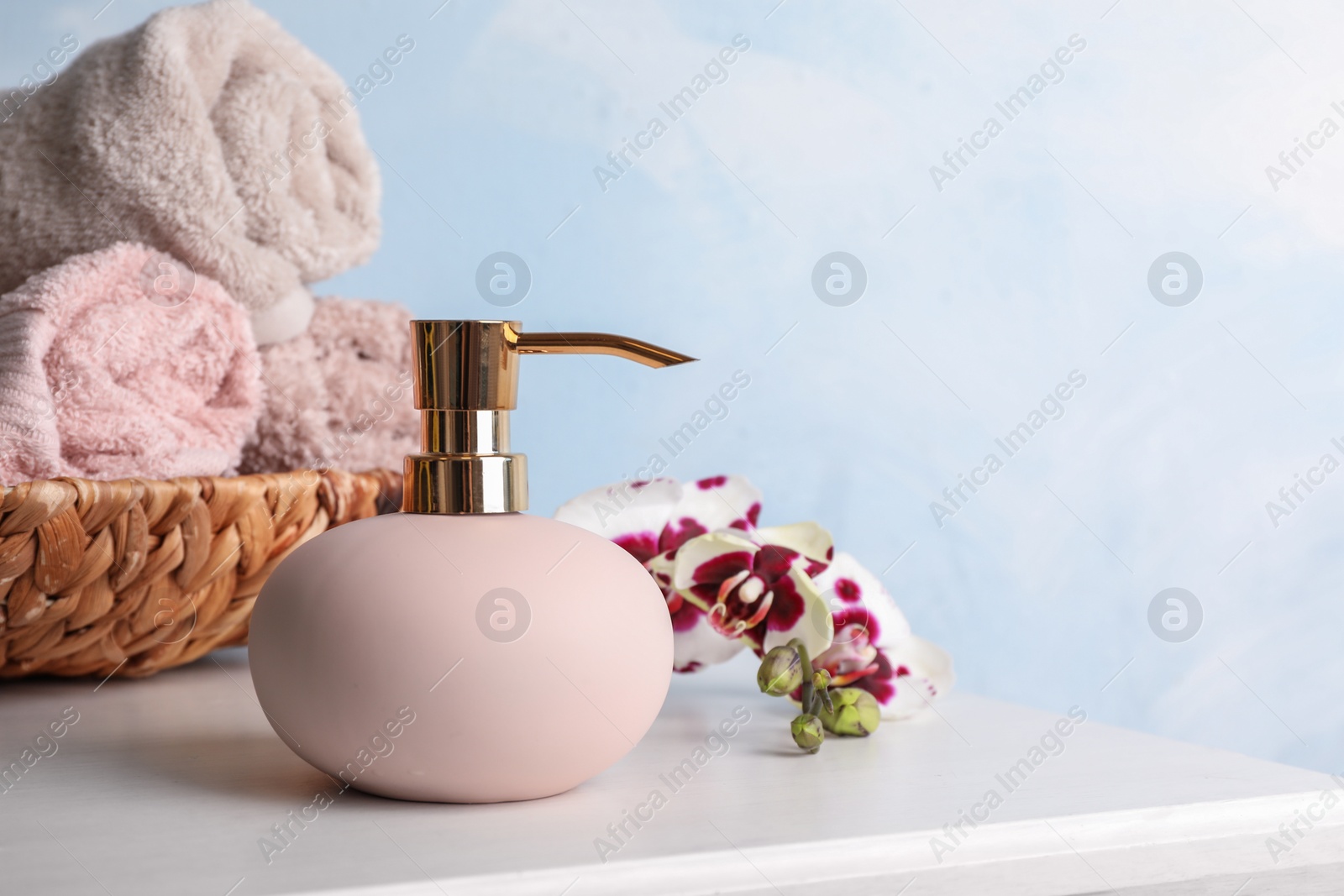 Photo of Stylish soap dispenser, towels in wicker basket and flowers on table. Space for text