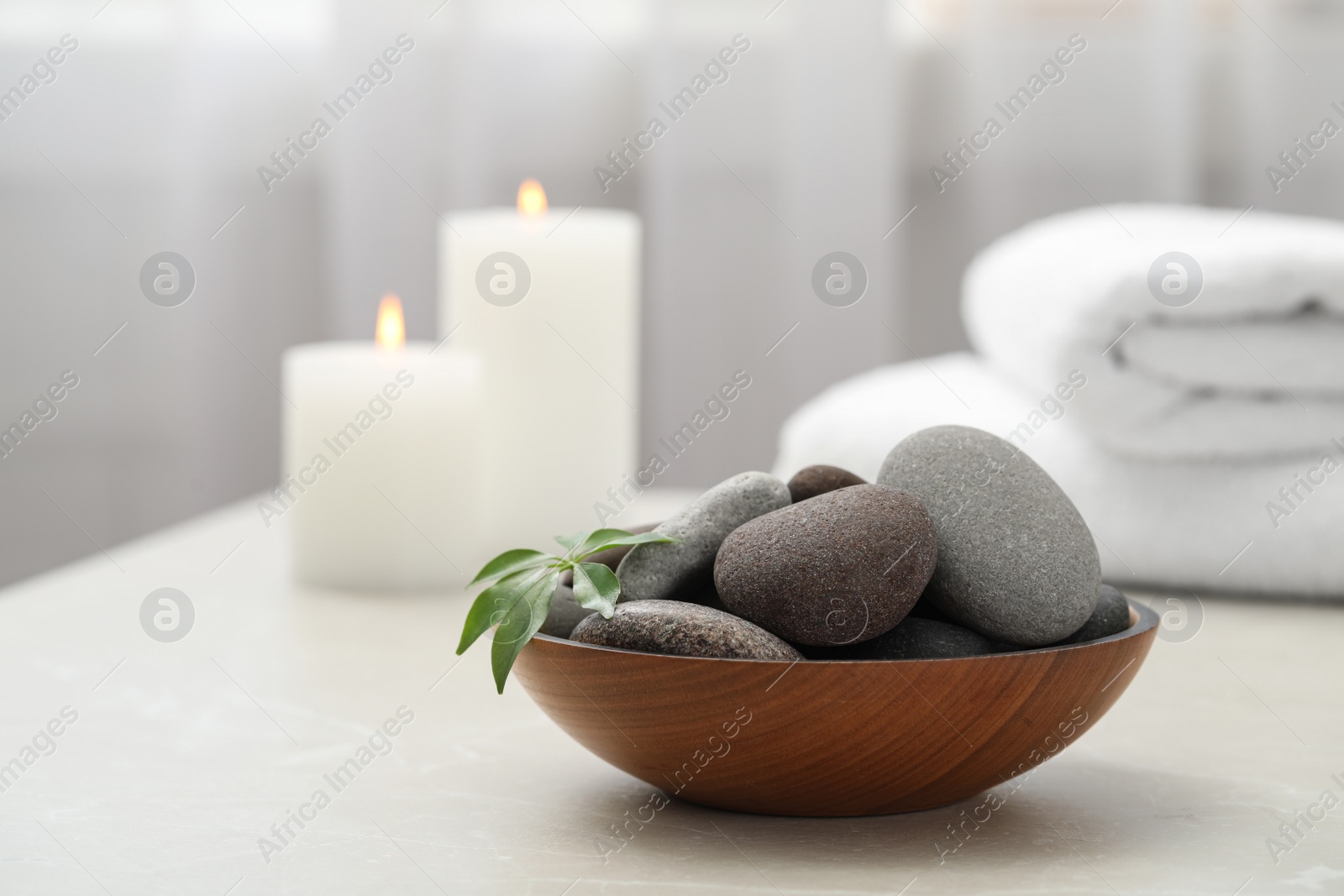 Photo of Spa stones in wooden bowl on white table indoors