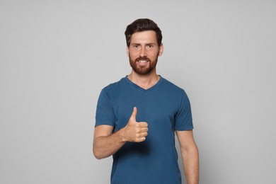 Handsome bearded man showing thumb up on light grey background