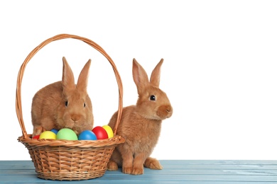 Photo of Cute fluffy bunnies and wicker basket with Easter eggs on light blue wooden table
