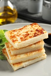 Photo of Delicious turnip cake with arugula and soy sauce on plate, closeup