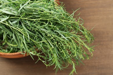 Photo of Bunch of fresh tarragon in bowl on wooden table, closeup