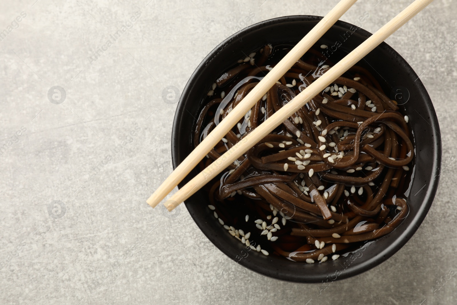 Photo of Tasty buckwheat noodles (soba) with sauce in bowl and chopsticks on light table, top view. Space for text