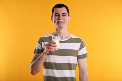 Photo of Happy man with milk mustache holding glass of tasty dairy drink on orange background