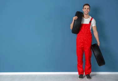 Photo of Young mechanic in uniform with car tires near color wall