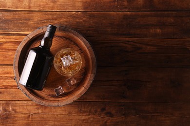 Whiskey with ice cubes in glass, bottle and barrel on wooden table, top view. Space for text