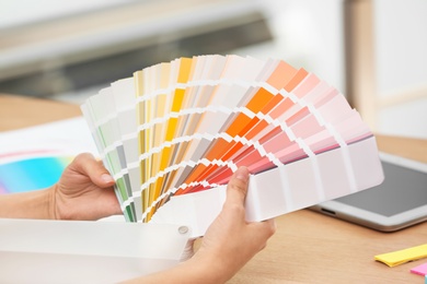 Photo of Designer with paint color palette samples at table, closeup