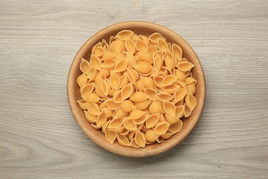 Photo of Raw conchiglie pasta in bowl on light grey wooden table, top view
