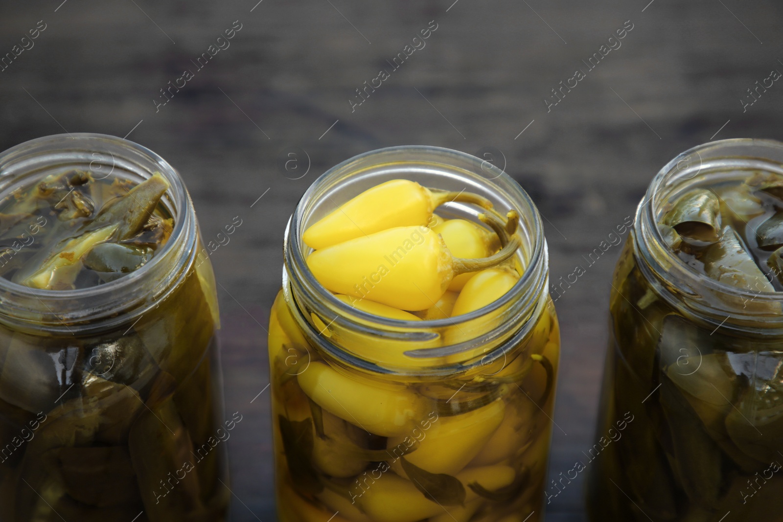 Photo of Glass jars of pickled green and yellow jalapeno peppers on wooden table, closeup