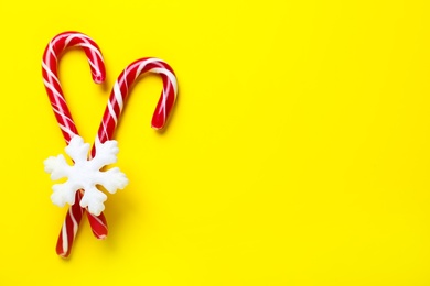 Sweet Christmas candy canes and snowflake on yellow background, flat lay. Space for text