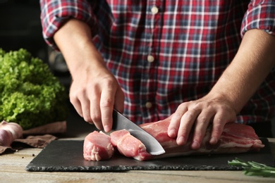 Man cutting fresh raw meat on wooden table, closeup