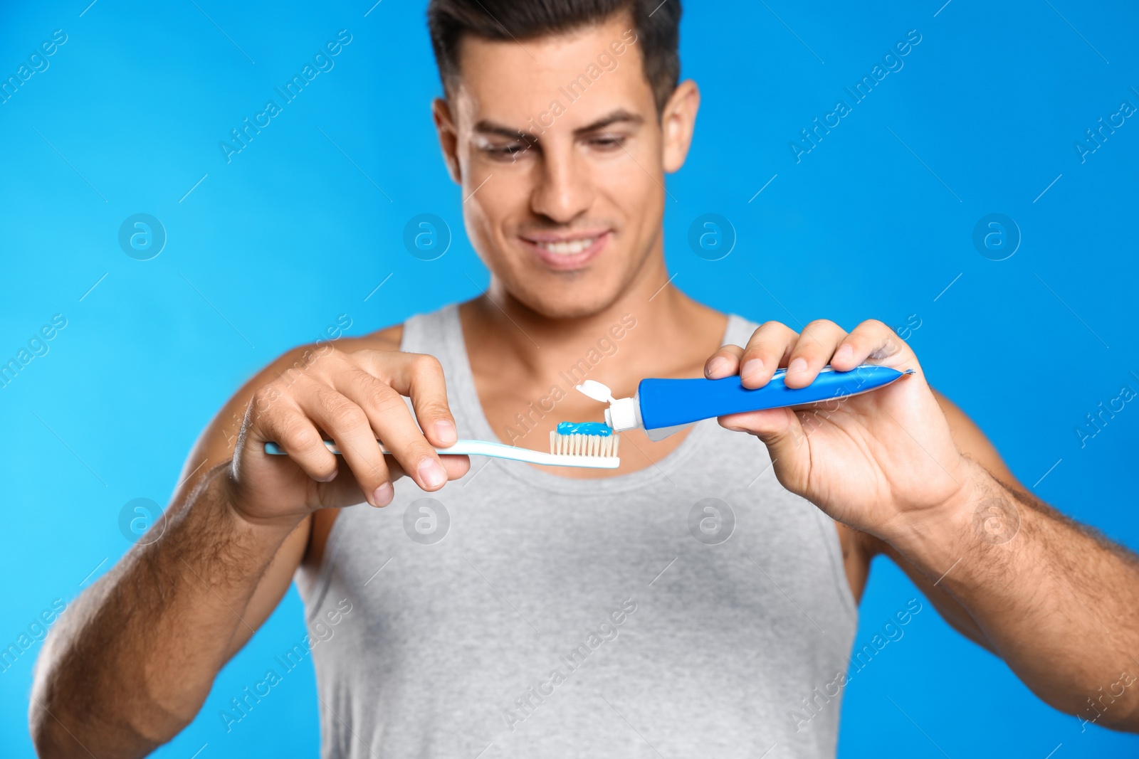 Photo of Man applying toothpaste on brush against blue background
