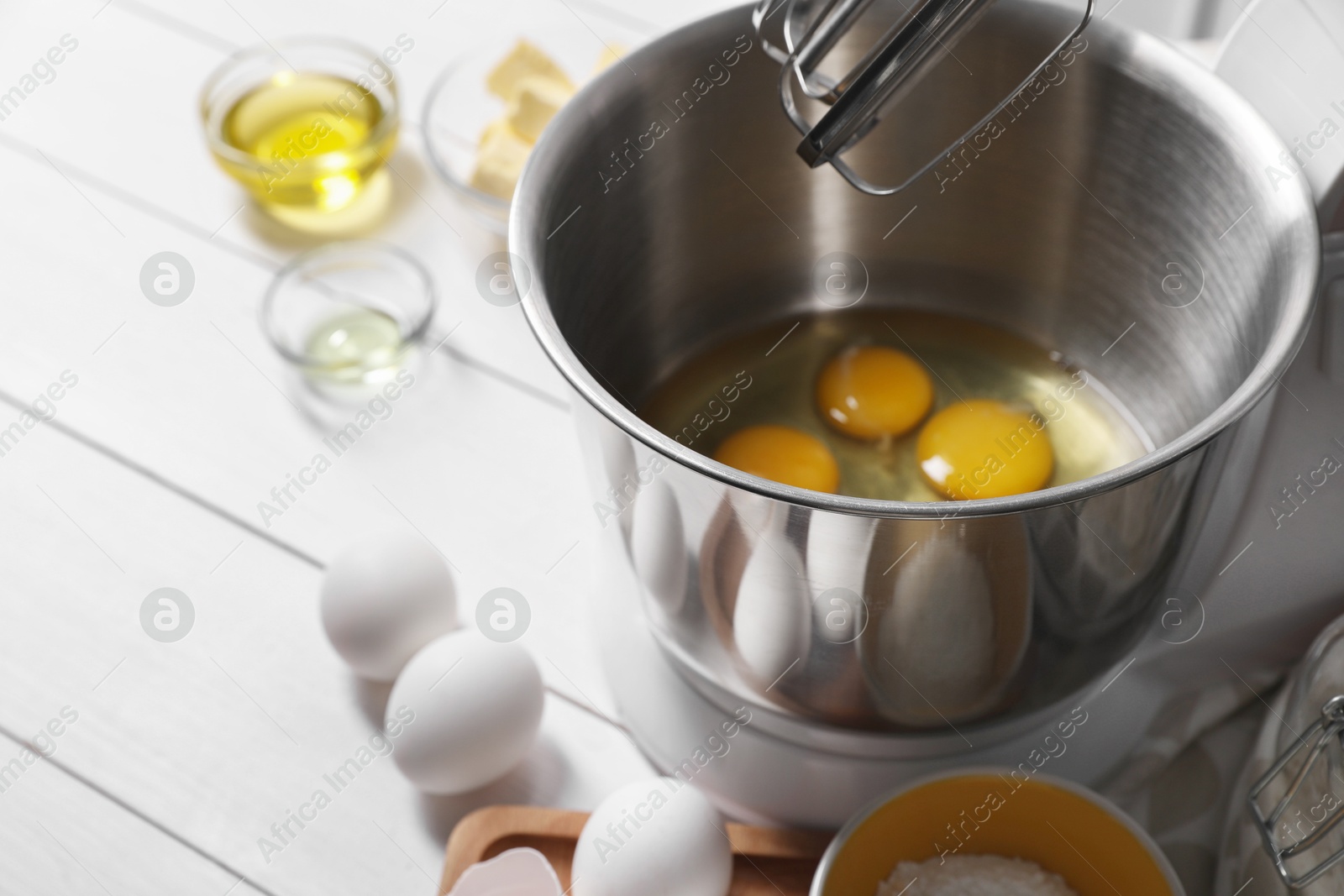 Photo of Making dough. Raw eggs in bowl of stand mixer and ingredients on white wooden table