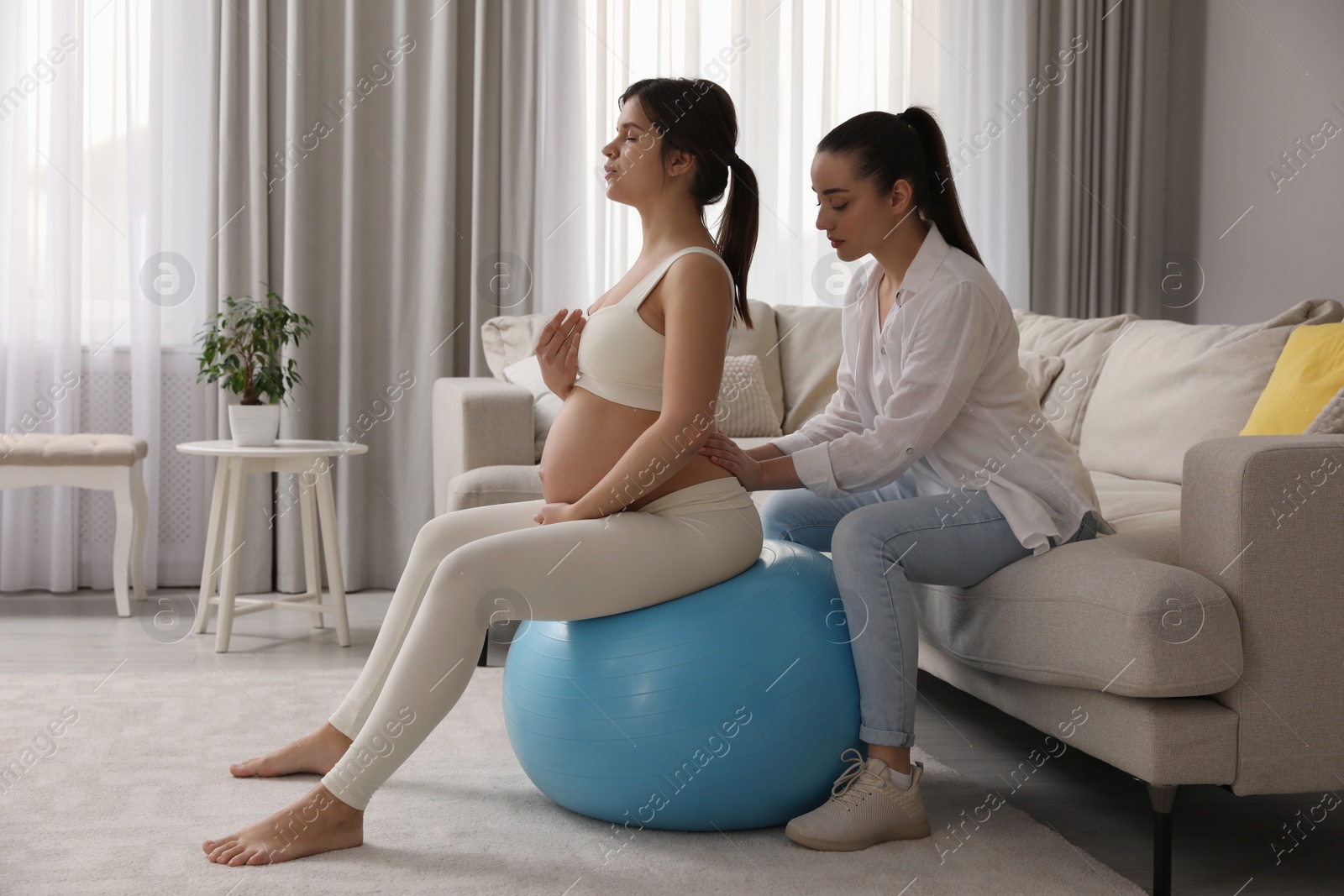 Photo of Doula working with pregnant woman in living room. Preparation for child birth