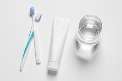 Plastic toothbrushes with paste and glass of water on white background, top view