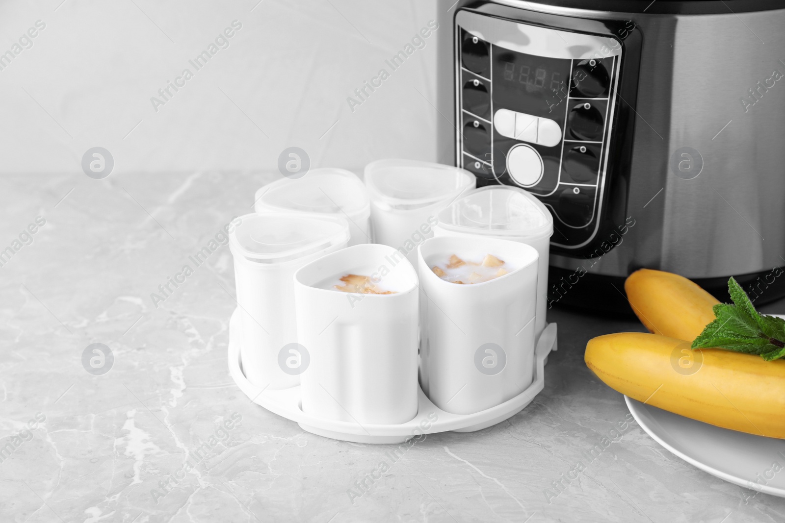 Photo of Cups of yogurt with bananas and multi cooker on table. Space for text