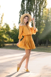 Photo of Beautiful young woman in stylish yellow dress and straw hat outdoors