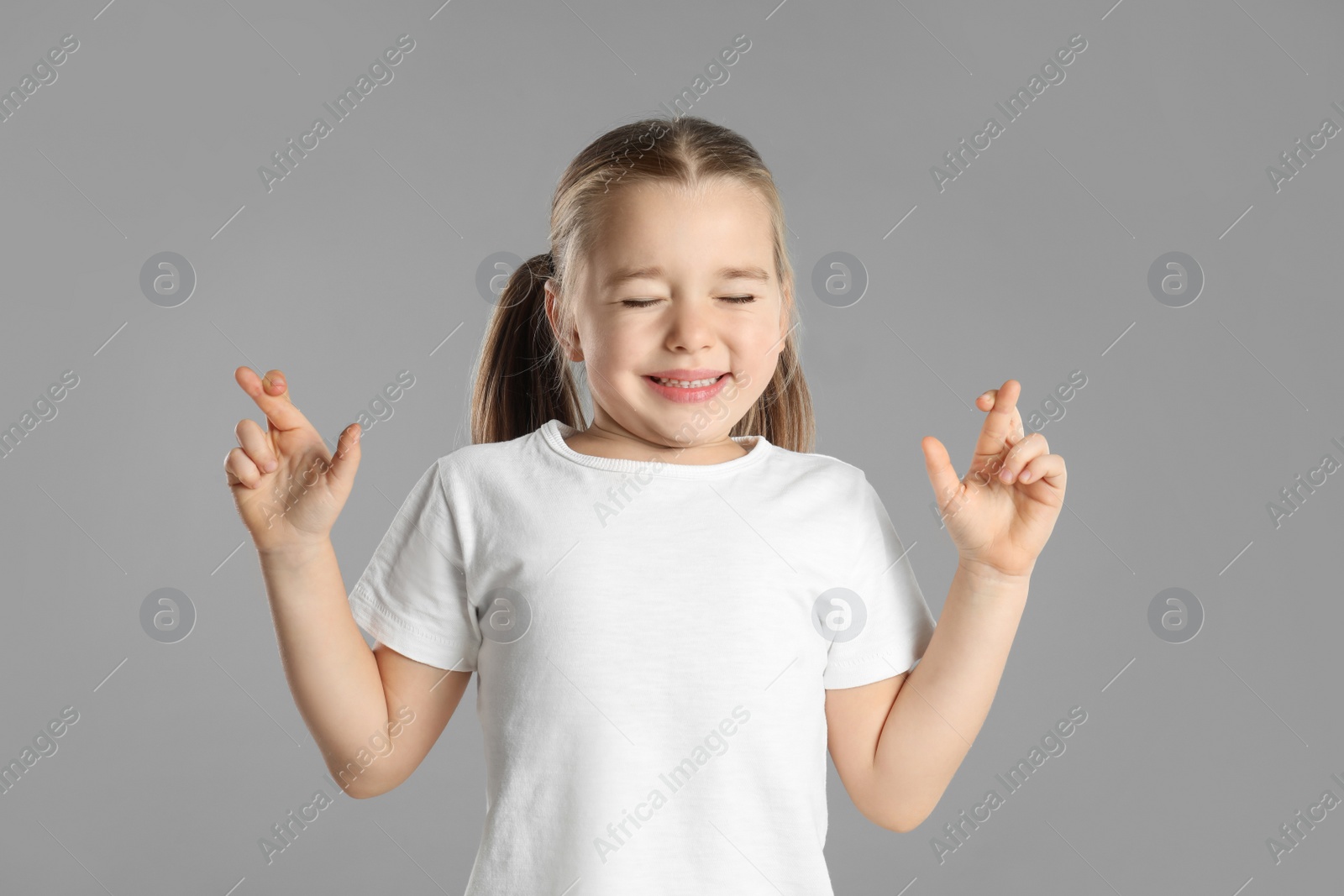 Photo of Child with crossed fingers on light grey background. Superstition concept