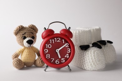 Photo of Alarm clock, toy bear and baby booties on white background. Time to give birth