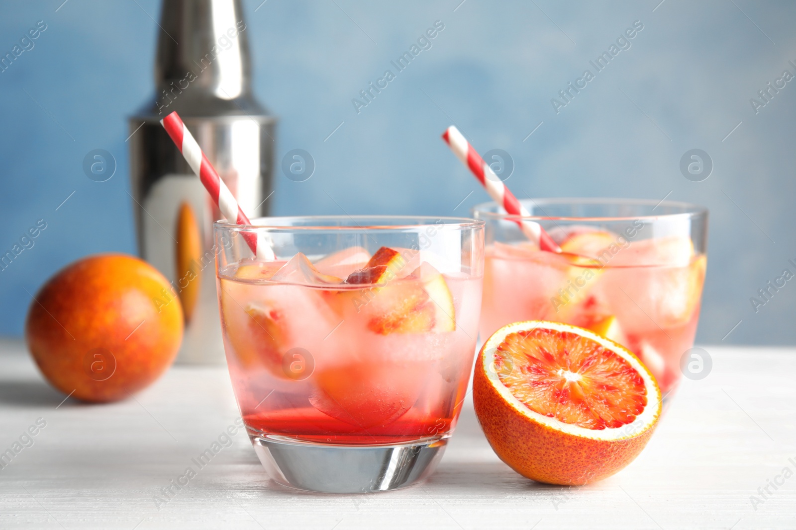 Photo of Glasses of tropical cocktail with ice cubes on table against color background