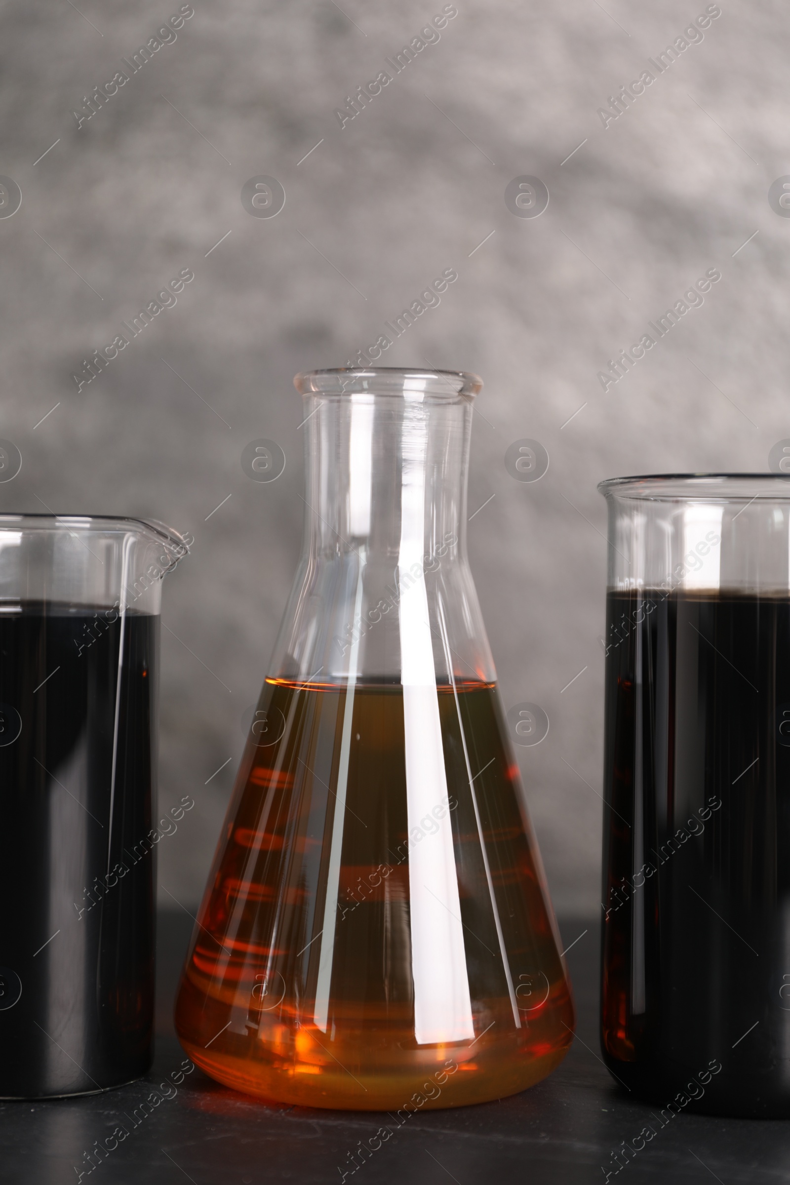 Photo of Beakers and flask with different types of oil on grey textured table