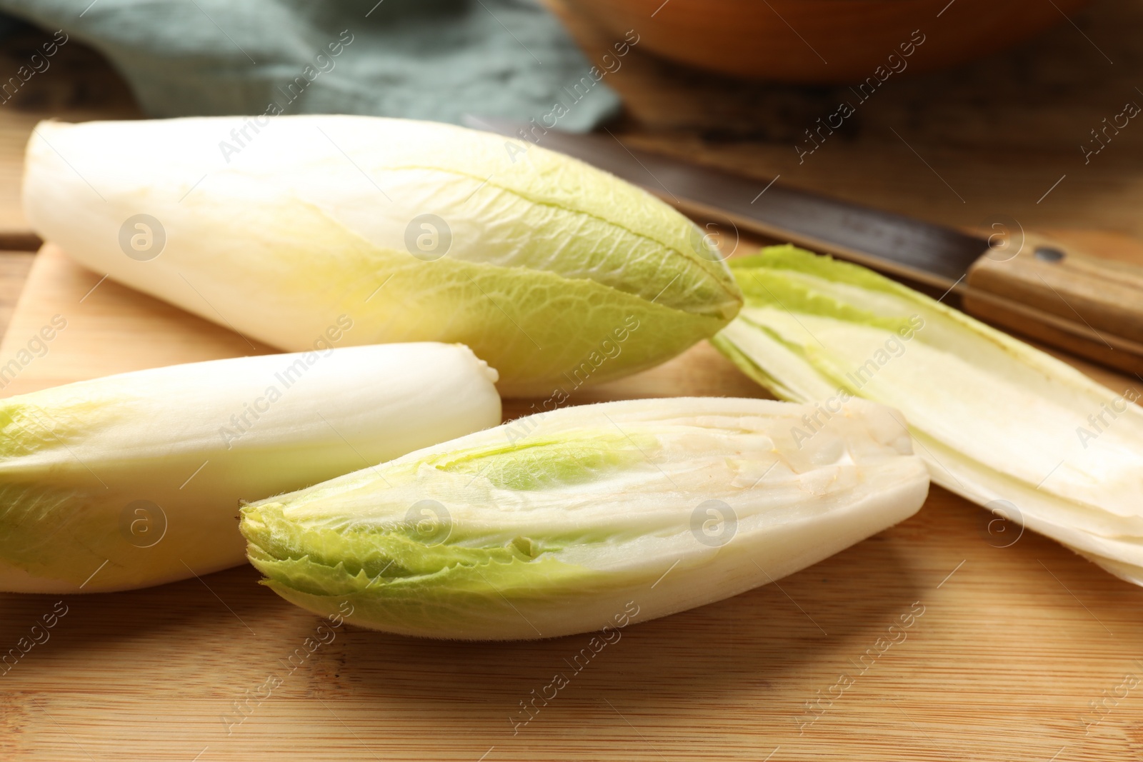 Photo of Fresh raw Belgian endives (chicory), wooden board and knife on table, closeup