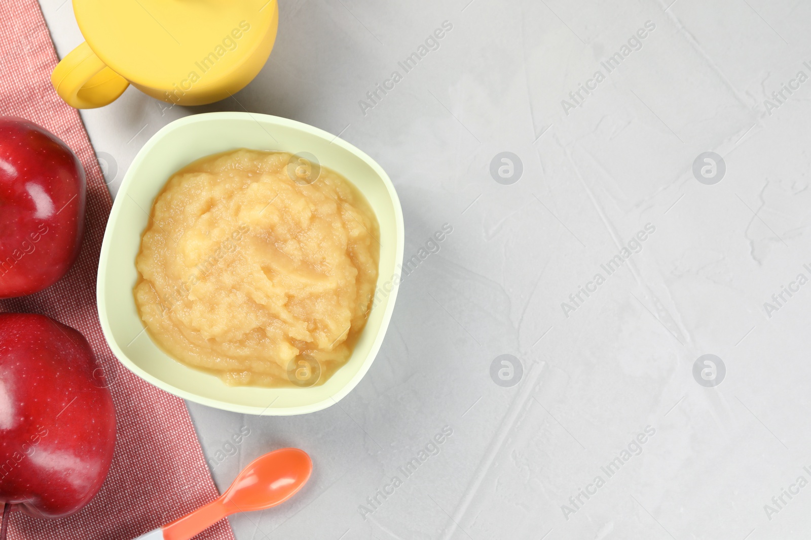 Photo of Healthy baby food. Bowl with delicious apple puree and fruits on light grey table, flat lay. Space for text