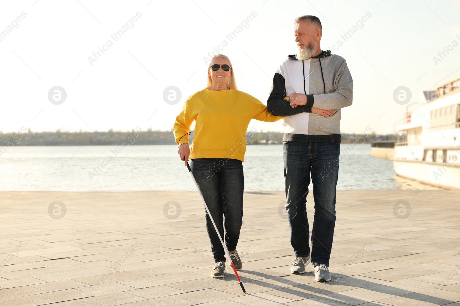 Photo of Mature man helping blind person with long cane in city