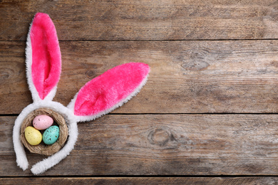 Headband with bunny ears, painted eggs and space for text on wooden background, flat lay. Easter holiday