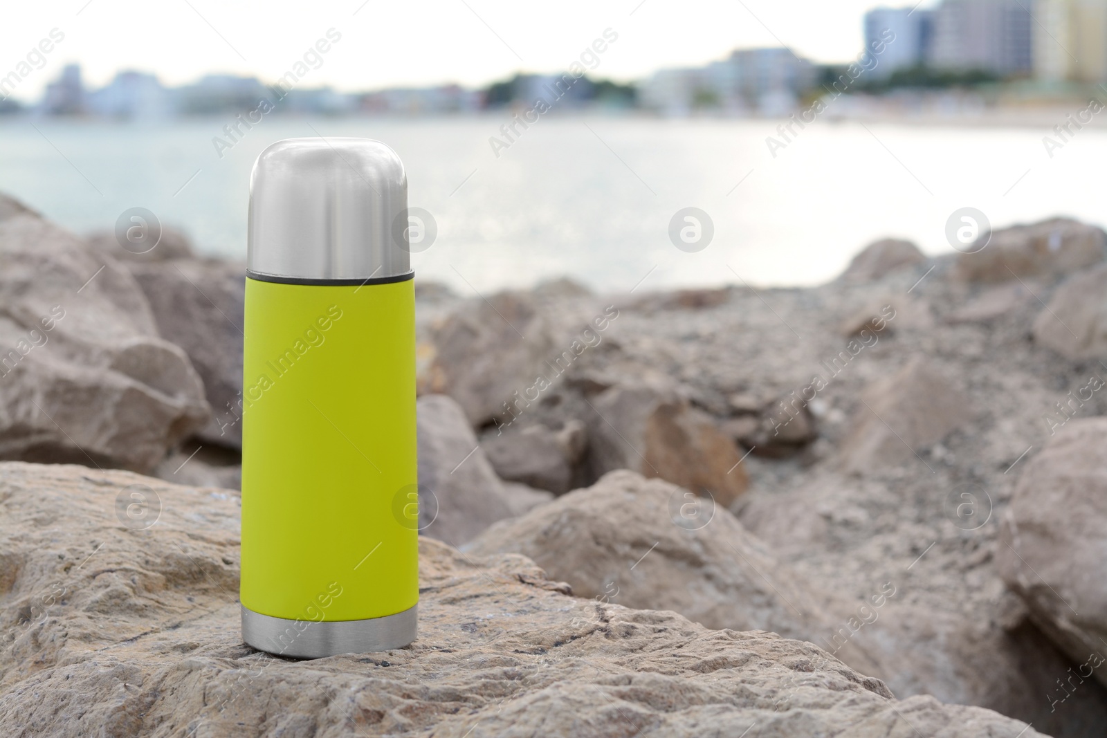 Photo of Metallic thermos with hot drink on stone near sea, space for text