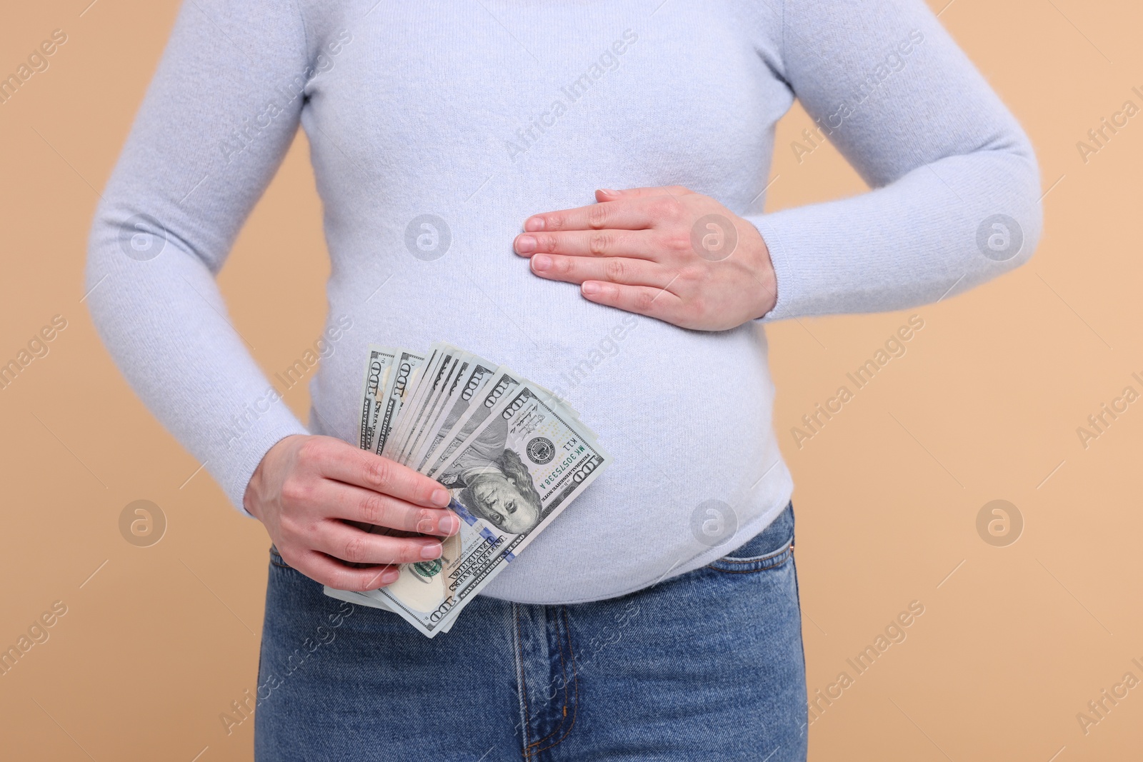 Photo of Surrogate mother. Pregnant woman with dollar banknotes on beige background, closeup