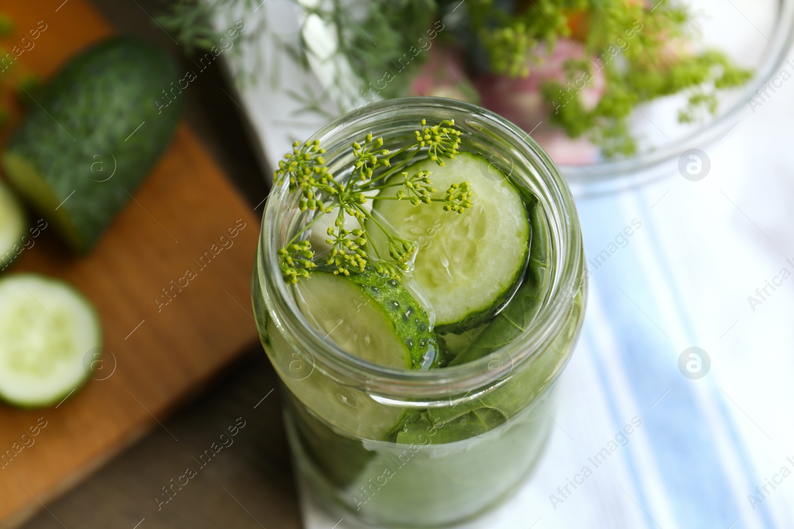 Photo of Glass jar with cucumber slices, dill and brine on table, closeup. Pickling recipe