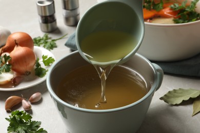 Photo of Pouring hot delicious bouillon into cup on light grey table, closeup