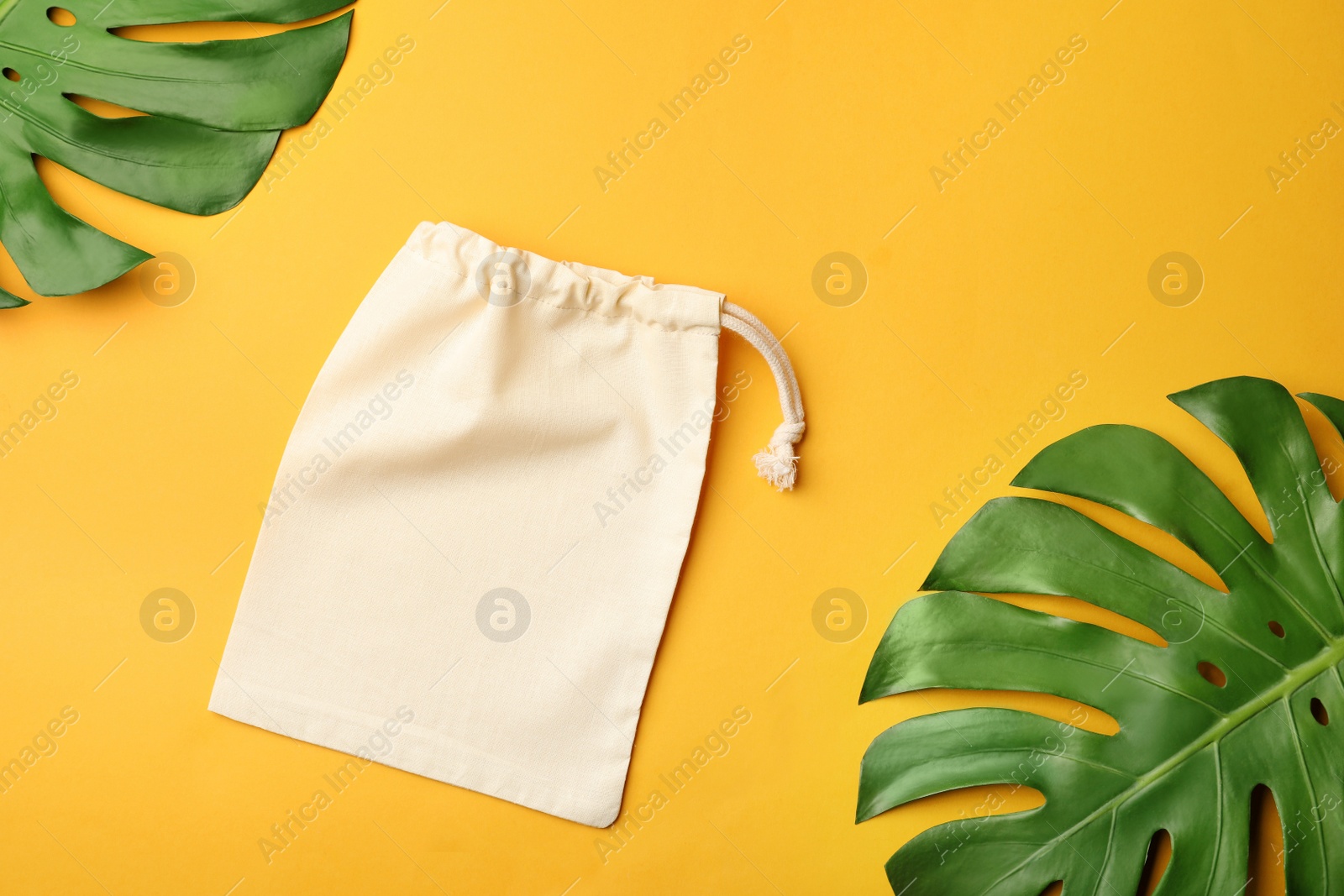 Photo of Cotton eco bag and leaves on yellow background, flat lay