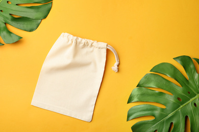 Photo of Cotton eco bag and leaves on yellow background, flat lay