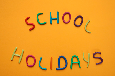 Phrase School Holidays made of modeling clay on orange background, top view