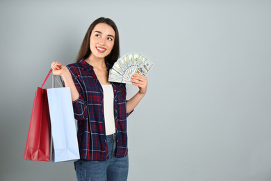 Photo of Young woman with money and shopping bags on light grey background. Space for text