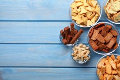 Photo of Different crispy rusks in bowls on light blue wooden table, flat lay. Space for text