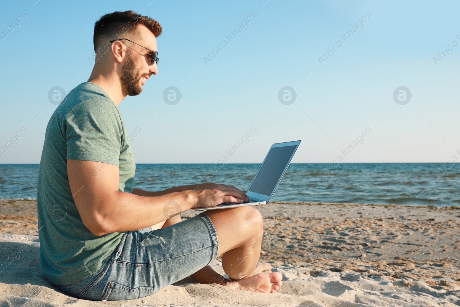 Photo of Man working with modern laptop on beach