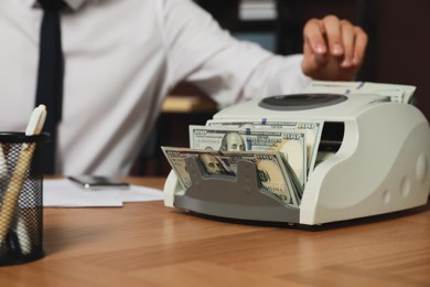 Photo of Man putting money into banknote counter at wooden table indoors, closeup