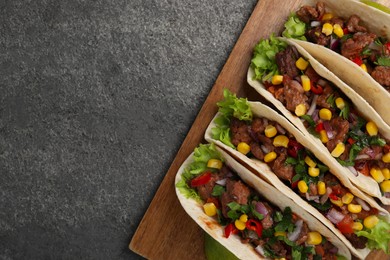 Delicious tacos with meat and vegetables on gray textured table, top view. Space for text