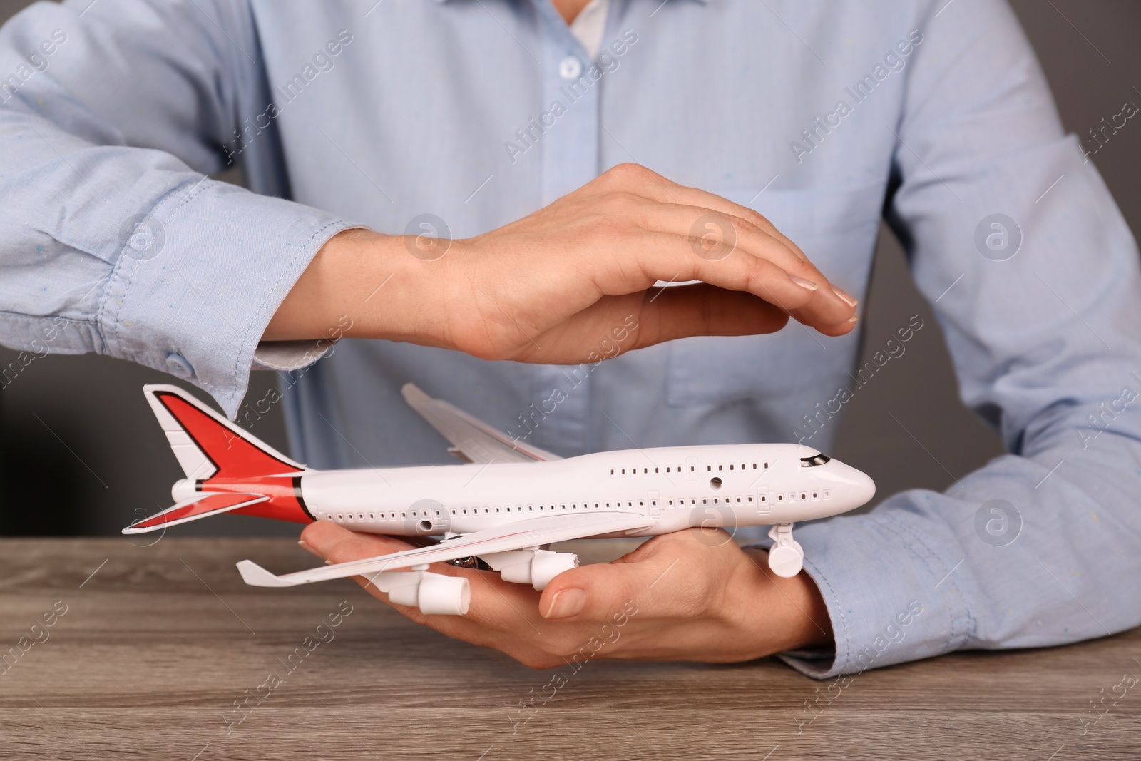 Photo of Insurance agent covering toy plane at table, closeup. Travel safety concept