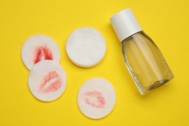 Bottle of makeup remover, clean and dirty cotton pads on yellow background, flat lay